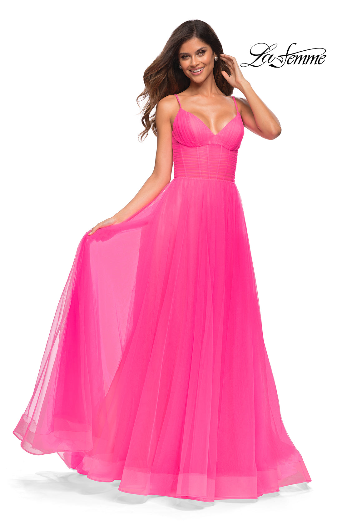 A woman models the La Femme Long Neon Pink Prom Ball Gown with Pockets, featuring a fitted bodice and flowing skirt, posed against a white background to highlight this vibrant formal evening dress.